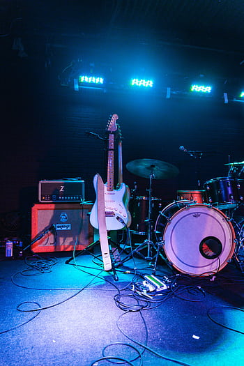 Electric guitar and drum set on an illuminated live music stage, ready for performance. HD phone wallpaper