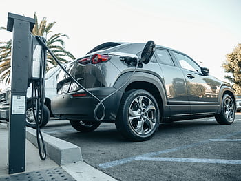 Modern electric vehicle charging at an outdoor station in daylight. HD wallpaper