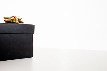 Minimalist black gift box adorned with a gold ribbon on a white background, perfect for celebrations. HD wallpaper