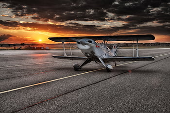 A classic biplane rests on the runway against a stunning sunset backdrop. HD wallpaper