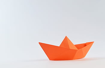 Minimalist of an orange origami paper boat on a white background, perfect for creativity and craft concepts. HD wallpaper