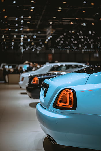 Rear view of luxury cars lined up at an indoor auto show with bright lighting. HD phone wallpaper