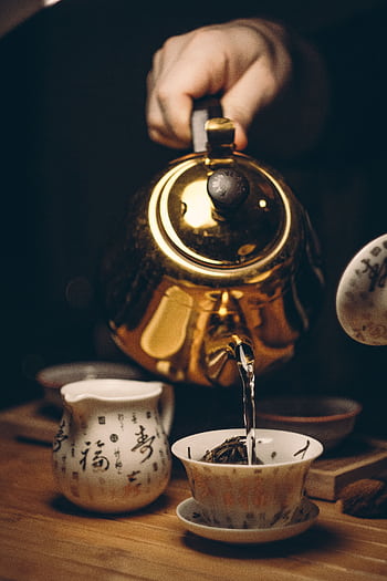 Close-up of a golden teapot pouring tea into a cup with Chinese calligraphy. HD phone wallpaper