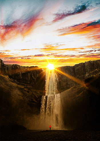 A stunning sunset casting vibrant colors over a powerful waterfall surrounded by cliffs. HD phone wallpaper