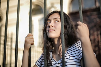 A teenage girl looks thoughtfully through bars, symbolizing hope and dom. HD wallpaper