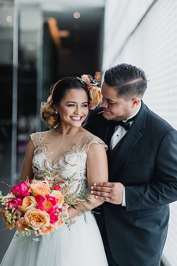 Joyful wedding portrait of a young couple indoors, holding a vibrant bouquet. HD phone wallpaper
