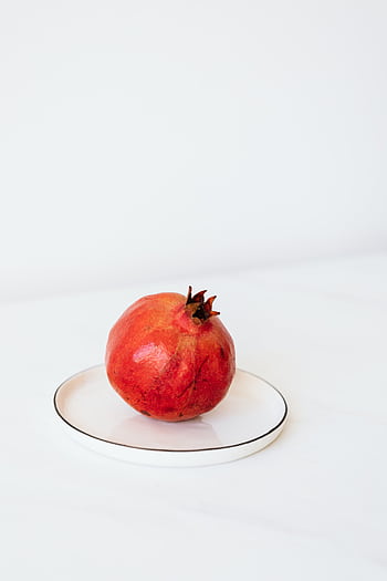 A fresh red pomegranate placed on a white plate with a simple, elegant composition. HD phone wallpaper