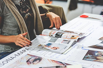 Detail shot of a woman browsing through magazines on a table filled with printed materials. HD wallpaper