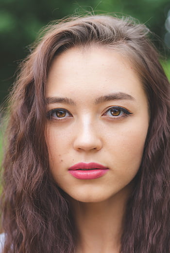 Close-up of a woman with natural makeup and loose waves in an outdoor setting. HD phone wallpaper