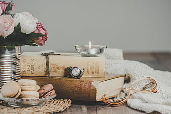 Vintage still life with books, macarons, candle, and flowers on a cozy table. HD wallpaper
