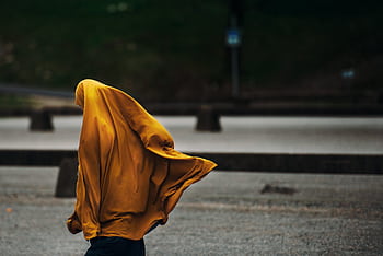 A woman walking in an outdoor setting with a flowing yellow hijab, capturing a dynamic street moment. HD wallpaper