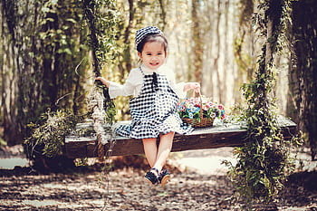 Adorable child smiling on a wooden swing with a basket of flowers in a sunny park. HD wallpaper