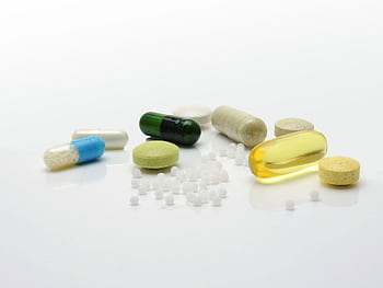 Close-up of various pills and capsules on a white surface, representing healthcare. HD wallpaper