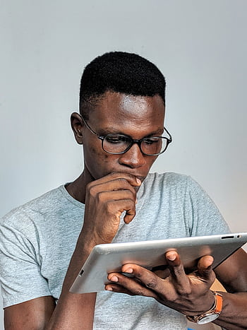 Young man wearing glasses engrossed in using a tablet device indoors. HD phone wallpaper