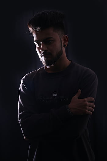 A young man standing with arms crossed, captured in shadowy lighting for a dramatic effect. HD phone wallpaper