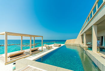 Stunning view of a luxury resort in Maldives with an infinity pool overlooking the ocean. HD wallpaper