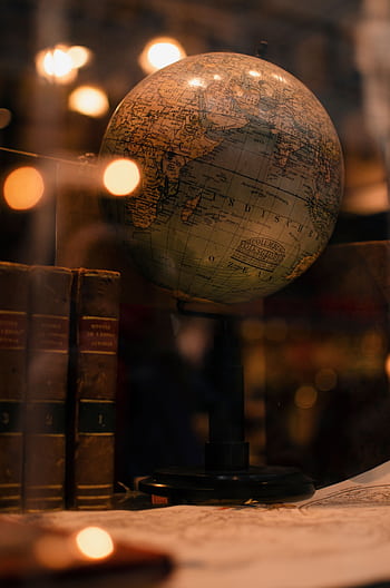 A vintage globe with books on a desk, highlighted by warm light through glass. HD phone wallpaper