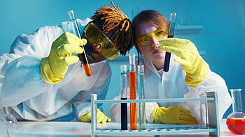 Two scientists in protective gear analyzing test tubes in a laboratory setting. HD wallpaper