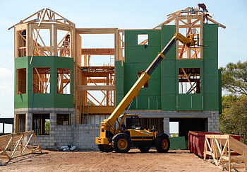 A multi-story wooden house under construction using a crane on a sunny day. HD wallpaper