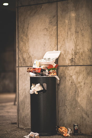 A trash can overflowing with garbage in an urban setting, against a concrete wall. HD phone wallpaper