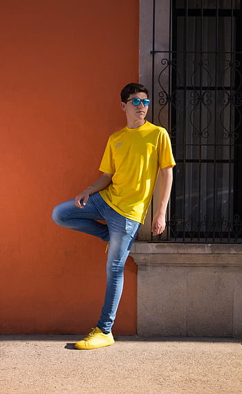 Youthful fashion model posing against a vivid orange wall in summer attire. HD phone wallpaper