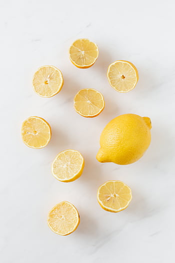 A flat lay of whole and sliced fresh lemons on a clean marble surface. HD phone wallpaper