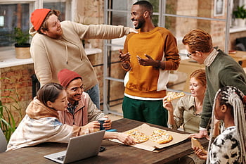 A group of diverse friends laughing and enjoying pizza together indoors. HD wallpaper
