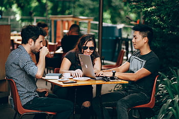 A group of young adults working on a laptop at an outdoor coffee shop, enjoying teamwork and collaboration. HD wallpaper