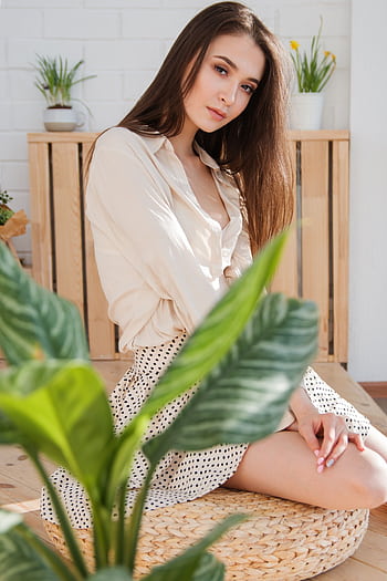 Portrait of a young woman seated indoors surrounded by plants, exuding elegance and grace. HD phone wallpaper
