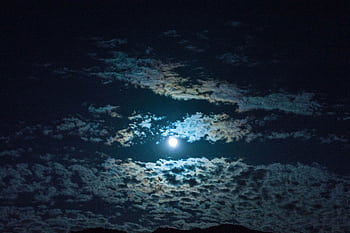 Capture of a dramatic night sky featuring a bright full moon surrounded by scattered clouds, creating an ethereal atmosphere. HD wallpaper