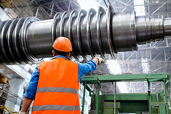 Engineer in high visibility vest and hard hat inspecting large machinery in factory setting. HD wallpaper