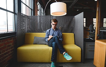 Young man writing on a notebook while sitting on a couch in a modern coworking space. HD wallpaper