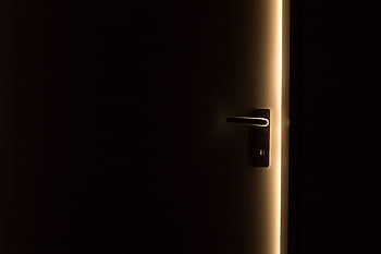 A dark room with a door slightly ajar, revealing a glowing light through the opening. HD wallpaper
