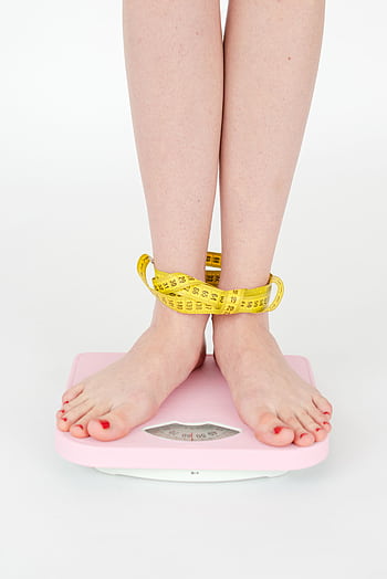 Close-up of a woman's feet on a pink scale wrapped in measuring tape, symbolizing weight management. HD phone wallpaper