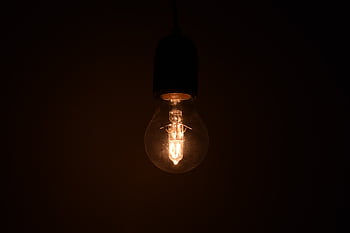 Close-up view of an illuminated light bulb glowing in a dark environment, emitting warm light. HD wallpaper