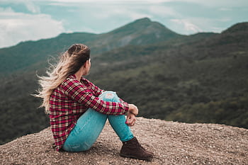 A woman in casual wear enjoys solitude on a scenic Brazilian mountain, embracing a moment of reflection. HD wallpaper