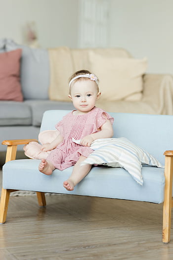 Cute baby girl in a pink dress sitting on a sofa, exuding happiness and innocence indoors. HD phone wallpaper
