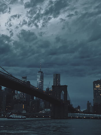 A dramatic view of the Brooklyn Bridge and New York City skyline under dark, moody clouds at dusk. HD phone wallpaper