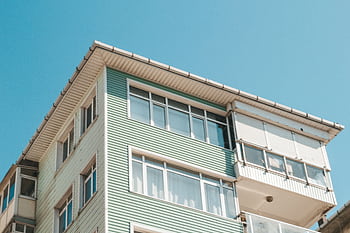 Low angle view of a modern apartment building exterior with glass windows under a clear blue sky. HD wallpaper