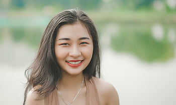 A cheerful young woman smiles brightly in an outdoor setting by the lake. HD wallpaper