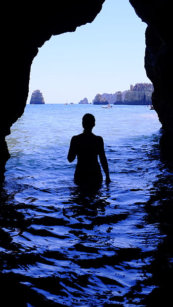 A captivating silhouette of a woman standing in a cave, gazing at the ocean vista beyond. HD phone wallpaper