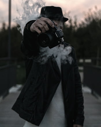 A mysterious figure holding a camera amidst smoke, creating an enigmatic atmosphere. HD phone wallpaper