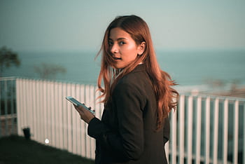 Stylish young woman holds smart with a scenic sea backdrop outdoors. HD wallpaper