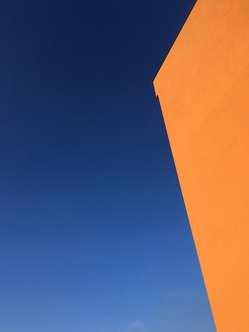 Striking minimalist composition featuring an orange building against a vivid blue sky. HD phone wallpaper