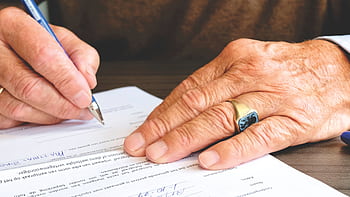 Close-up of a senior adult signing a legal document with a focus on hand and gold ring. HD wallpaper