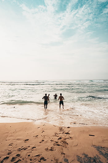 Three friends run into the ocean on a sunny day at a scenic beach in Bali. HD phone wallpaper