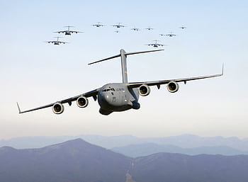 A formation of military cargo aircraft flying over a mountainous landscape, showcasing aviation power. HD wallpaper