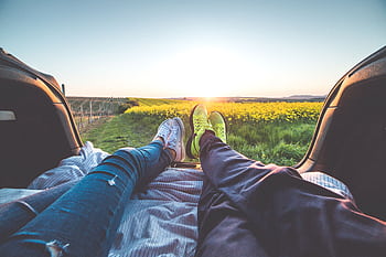 A couple relaxing in a car trunk enjoying a romantic sunset over fields. HD wallpaper