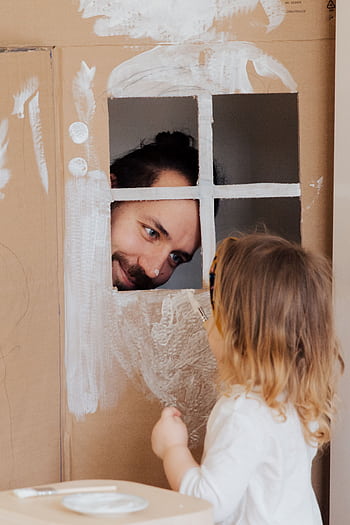 Father and child enjoy creative play with a cardboard house indoors. HD phone wallpaper