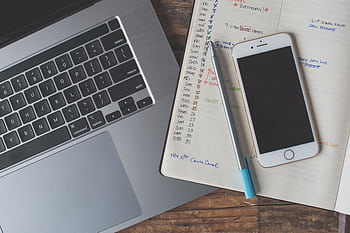 A workspace featuring a laptop, smart, and planner on a wooden desk, ideal for remote work. HD wallpaper